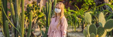 BANNER, Kaktüslerin arasında çölde pembe elbiseli, uzun ve şık bir kadın, COVID-19 Coronavirus sırasında tıbbi maske takıyor, Afrika 'da safari yapıyor, doğayı keşfediyor, güneşli