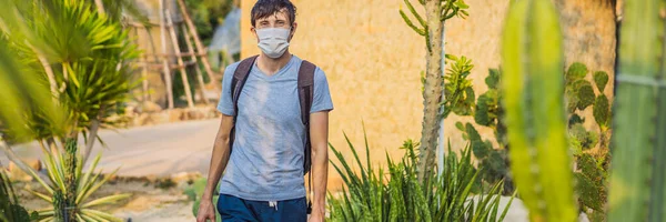 BANNER, LONG FORMAT Schöner, stylischer junger Mann in Wüste inmitten der Kakteen, trägt eine medizinische Maske während des COVID-19 Coronavirus, reist auf Safari durch Afrika, erkundet die Natur, sonniger Sommer, Reisende — Stockfoto