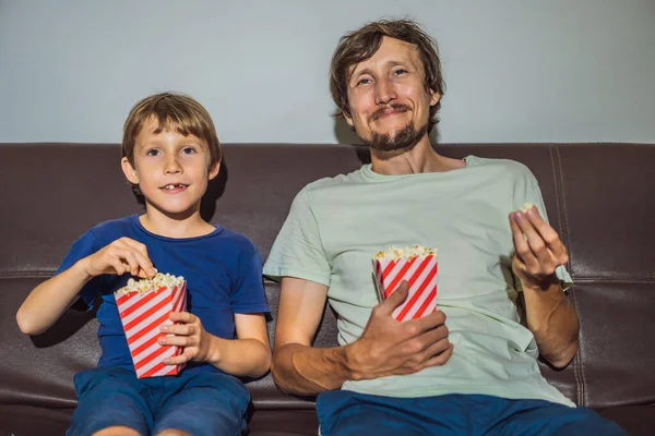 Father and son watching TV and eat popcort in evening at home