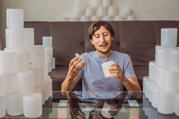 The man eats yogurt and is surrounded by many jars of yoghurt that he uses in a year. A huge amount of plastic food jars. Excessive consumption of plastic. Reduce, reuse, recycle — Stock Photo, Image