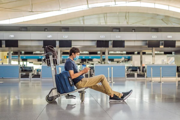 Man in mask at empty airport at check in in coronavirus quarantine isolation, returning home, flight cancellation, pandemic infection worldwide spread, travel restrictions and border shutdown