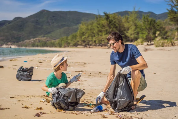 Vater und Sohn in Handschuhen säubern den Strand und sammeln Plastiktüten auf, die das Meer verschmutzen. Natürliche Erziehung der Kinder. Problem des verschütteten Mülls Müll am Strand Sand durch künstliche verursacht — Stockfoto