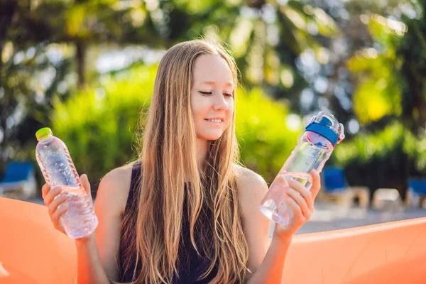 Summer lifestyle portrait of pretty girl sitting on the orange inflatable sofa selects a disposable bottle or reusable. zero waste on the beach of tropical island. Relaxing and enjoying life on air — Stock Photo, Image