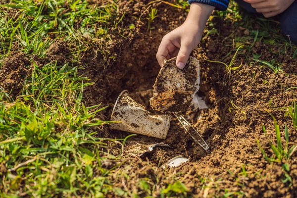 The boy plays recycling. He buries plastic disposable dishes and biodegradable dishes. After a few months, he dug up the dishes and saw that the biodegradable dishes began to decompose and plastic did — Stock Photo, Image