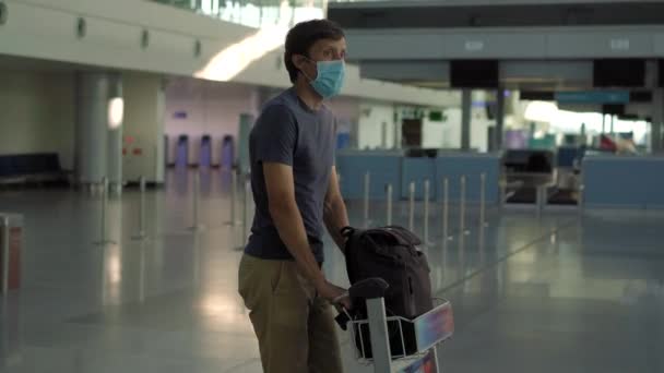 Mężczyzna w masce na pustym lotnisku podczas odprawy w izolacji od koronawirusów, powrót do domu, anulowanie lotu, rozprzestrzenienie się pandemii na całym świecie, ograniczenia podróży i zamknięcie granicy — Wideo stockowe
