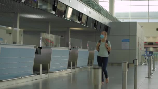 Kvinna i mask vid tom flygplats vid incheckning i karantänisolering av coronavirus, hemresa, inställda flygningar, pandemisk infektion över hela världen, reserestriktioner och stängning av gränser — Stockvideo