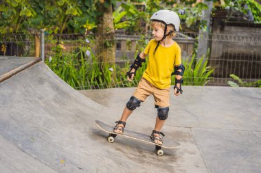 Kasklı ve dizlikli atletik çocuk kaykay yapmayı kaykay parkında öğreniyor. Çocuk eğitimi, spor