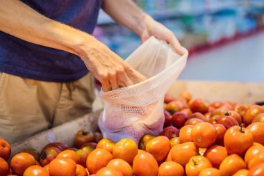 Adam süpermarkette plastik torba kullanmadan domates seçiyor. Sebze almak için tekrar kullanılabilir çanta. Sıfır atık