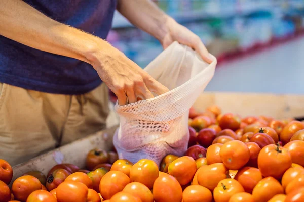 El hombre elige tomates en un supermercado sin usar una bolsa de plástico. Bolsa reutilizable para comprar verduras. Concepto de cero residuos — Foto de Stock