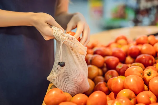 Una mujer elige tomates en un supermercado sin usar una bolsa de plástico. Bolsa reutilizable para comprar verduras. Concepto de cero residuos — Foto de Stock