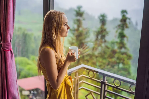 Молодая женщина держит чашку кофе, сидя на стуле на балконе, глядя на горы и зеленую природу. Женщина в Сапе в тумане, Северо-Западный Вьетнам. Концепция путешествия во Вьетнам. Наследие ЮНЕСКО — стоковое фото