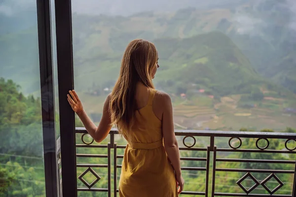 Eine junge Frau hält eine Kaffeetasse in der Hand, während sie auf einem Stuhl auf dem Balkon sitzt und die Berge und die grüne Natur betrachtet. Frau in Sapa im Nebel, Nordwest-Vietnam. Vietnam Reisekonzept. UNESCO-Weltkulturerbe — Stockfoto