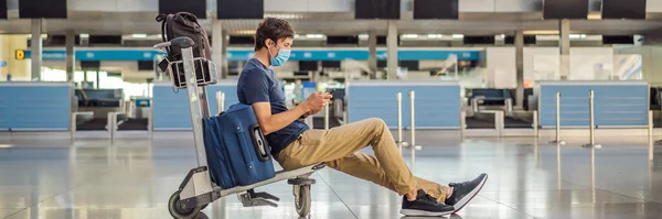 BANNER, LONG FORMAT Mann mit Maske auf leerem Flughafen beim Check-in in Coronavirus-Quarantäne-Isolation, Heimkehr, Flugausfall, weltweite Ausbreitung der Pandemie, Reisebeschränkungen und — Stockfoto