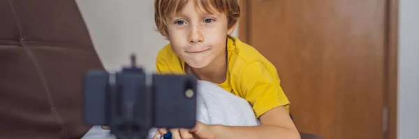 BANNER, LONGO FORMATO Manter-me ligado. Menino feliz olhando para seu telefone celular e sorrindo enquanto brincava com brinquedos. Um menino fala com alguém através de comunicação de vídeo durante o auto-isolamento devido a — Fotografia de Stock