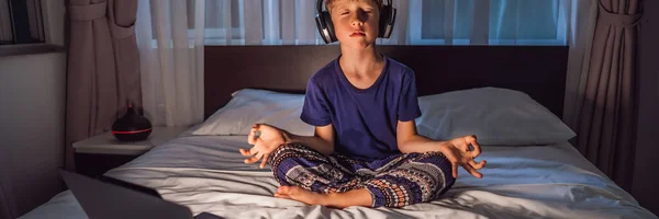 男の子は瞑想アプリを使ってベッドで瞑想します。スポーツ、テクノロジー、健康的なライフスタイルのコンセプト｜バナー、ロングフォーマット — ストック写真