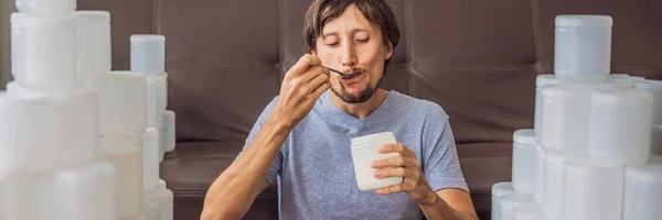 BANNER, LONG FORMAT The man eats yogurt and is surrounded by many jars of yoghurt that he uses in a year. A huge amount of plastic food jars. Excessive consumption of plastic. Reduce, reuse, recycle — Stock Photo, Image