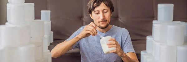 BANNER, LONG FORMAT The man eats yogurt and is surrounded by many jars of yoghurt that he uses in a year. A huge amount of plastic food jars. Excessive consumption of plastic. Reduce, reuse, recycle — Stock Photo, Image