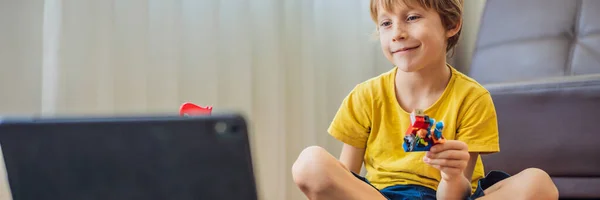 BANNER, LONG FORMAT Staying connected. Happy young boy looking at his mobile phone and smiling while playing with toys. A boy talks to someone via video communication during self-isolation due to