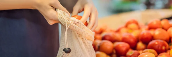 BANNER, LANG FORMAT Een vrouw kiest tomaten in een supermarkt zonder gebruik te maken van een plastic zak. Herbruikbare tas voor het kopen van groenten. Nul afvalconcept — Stockfoto