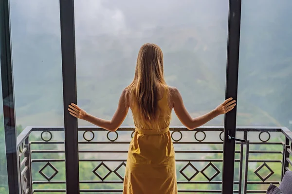 Balkonda sandalyeye oturmuş, dağlara ve yeşil doğaya bakan genç bir kadın kahve fincanı tutuyor. Sapa 'da siste, Kuzeybatı Vietnam' da bir kadın. Vietnam seyahat konsepti. UNESCO Mirası — Stok fotoğraf