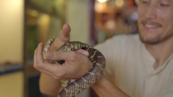 Um homem visita um café com animais exóticos. Café onde você pode entrar em contato com animais. Ele está tocando uma cobra. — Vídeo de Stock