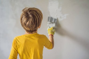 Çocuk evde tamirat yapıyor, çocuklara ellerinde bir spatulayla duvarları alçılamayı öğretiyor.