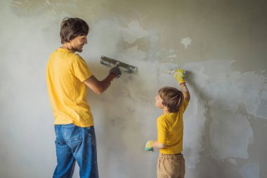 Oğluyla evde tamirat yapan bir adam, çocuklara ellerinde bir spatulayla duvarları alçılamayı öğretiyor.