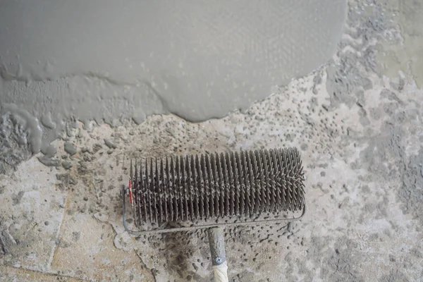 Gipser bei Bodenbelagsarbeiten mit selbstnivellierendem Zementmörtel, verwendet eine Nadelwalze — Stockfoto