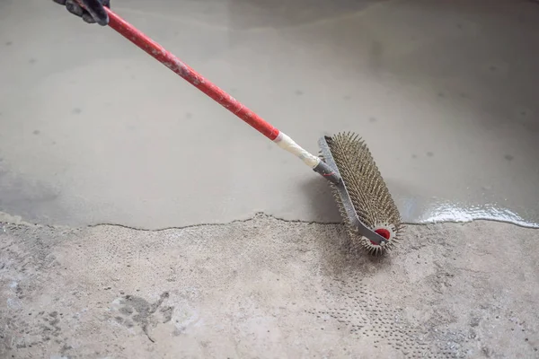 Plasterer during floor covering works with self-levelling cement mortar, uses a needle roller — Stock Photo, Image