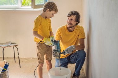 Oğluyla evde tamirat yapan bir adam, çocuklara ellerinde bir spatulayla duvarları alçılamayı öğretiyor.