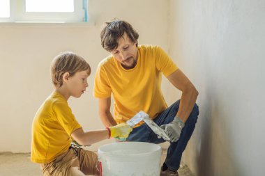 Oğluyla evde tamirat yapan bir adam, çocuklara ellerinde bir spatulayla duvarları alçılamayı öğretiyor.