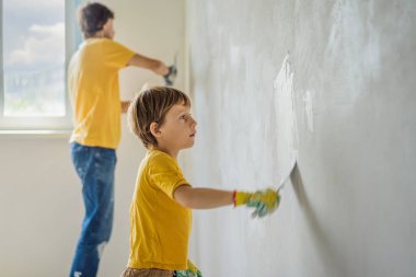 Oğluyla evde tamirat yapan bir adam, çocuklara ellerinde bir spatulayla duvarları alçılamayı öğretiyor.