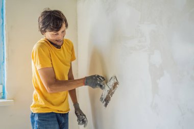 Sıvacı ev iyileştirme ustası macun bıçağıyla apartman duvarını doldurmaya çalışıyor.