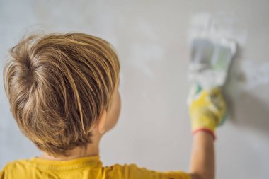 Çocuk evde tamirat yapıyor, çocuklara ellerinde bir spatulayla duvarları alçılamayı öğretiyor.