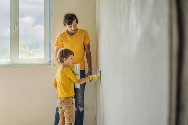 L'uomo con suo figlio fa riparazioni a casa, insegna ai bambini a intonacare le pareti con una spatola in mano. — Foto Stock