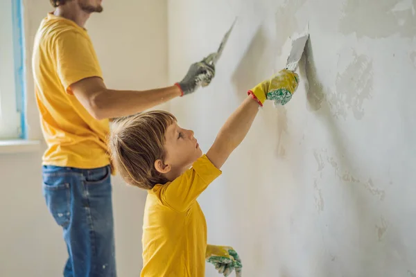 Oğluyla evde tamirat yapan bir adam, çocuklara ellerinde bir spatulayla duvarları alçılamayı öğretiyor. — Stok fotoğraf