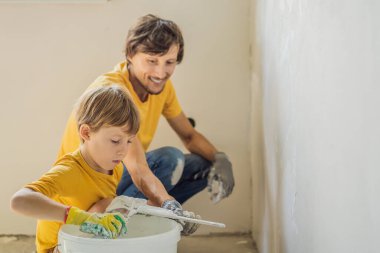 Oğluyla evde tamirat yapan bir adam, çocuklara ellerinde bir spatulayla duvarları alçılamayı öğretiyor.