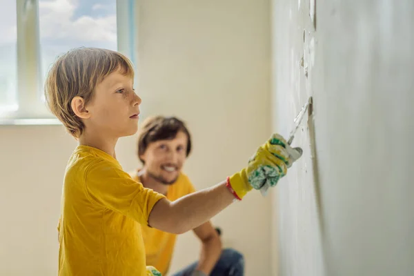 El hombre con su hijo hace reparaciones en casa, enseña a los niños a enlucir las paredes con una espátula en las manos —  Fotos de Stock