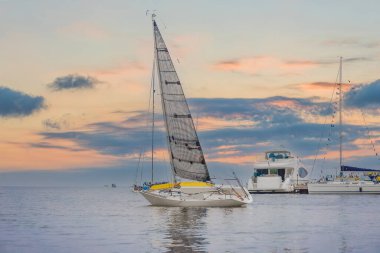 Günbatımına karşı yat sürüyor. Ufuk çizgisi yelkenli ve gün batımı silueti olan tatil yaşam tarzı manzarası. Yat turizmi - deniz akşam yürüyüşü. Günbatımında lüks bir yatta romantik bir gezi.