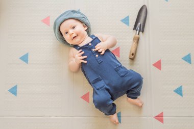 Yanında küçük bir bahçe küreği olan küçük bir bahçıvan gibi giyinmiş sevimli bir bebek. Bahçıvanlık kavramı, doğa bağlantısı ve çocukluk hayalgücü..