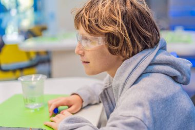 Güvenlik gözlüğü takan genç çocuk, STEM eğitimini, merakı ve bilimsel keşiflerin heyecanını temsil eden kimya deneyleri yapmaya hazırlanıyor..