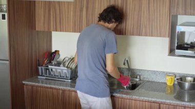 Genç bir adam mutfakta bulaşıkları yıkıyor, temizlik ve düzene odaklanıyor. Basit ve uyumlu bir ev yapımı, ev bakımı ve düzenli bir ev ortamı.