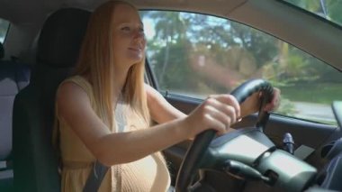 Hamile bir kadın güneşli bir günde araba kullanıyor. Güvenli seyahat ve hamilelik süresince bağımsızlık..