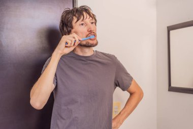 Modern bir banyoda dişlerini fırçalayan adam günlük hijyen ve sabah bakım rutini uyguluyor. Sağlıklı yaşam tarzı, tımar, temizlik ve diş bakımı konsepti.