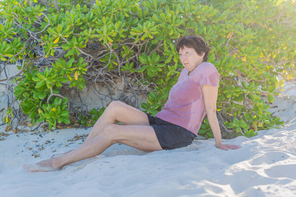 Пожилая женщина проводит время на пляже, наслаждаясь океанским бризом и теплым солнечным светом. Концепция активного старения, памятования, спокойствия, здорового образа жизни и мирного прибрежного образа жизни.