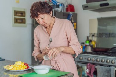 Mutfakta yemek pişiren yaşlı bir kadın, özenle ve neşeyle ev yemeği hazırlıyor. Sağlıklı yaşlanma, bağımsızlık, ev hayatı, aşçılık rutini ve evdeki aktif yaşlı yaşam tarzı kavramı.