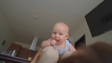 Gülümseyen baba, 1 yaşındaki çocuğunu yerde yatarken dizlerinin üzerinde sallıyor. Aile sevgisi kavramı, neşeli bağ ve neşeli babalık anları..