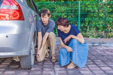 Genç bir adam, yaşlı bir kadına destek, şefkat ve gerçek yol yardımı göstererek yakınlarda otururken araba tekerleğini değiştirerek yardım ediyor. Aile bakımı, güvenlik, takım çalışması ve günlük sorunlar