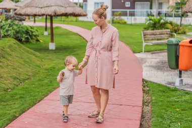 Güneşli bir parkta oğluyla yürüyen bir anne, açık havada güzel vakit geçiriyor. Sevgi bağı, ebeveyn bağı, boş zaman, doğa ve huzurlu günlük anlar kavramı..