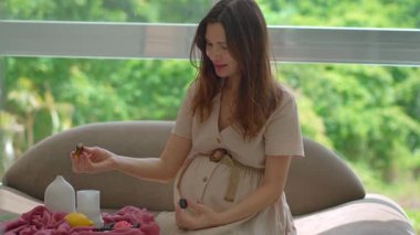 40 yaşından büyük hamile bir kadın parlak bir pencerenin yanında koltukta oturur ve aroma yayıcı kokusunun tadını çıkarır. Sağlık, rahatlama, hamilelik bakımı, sağlıklı yaşam tarzı ve ev huzuru kavramı.